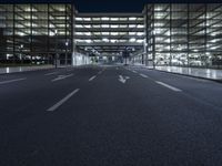 a empty empty city road at night with street lights shining behind it and an illuminated garage on the left side of the road