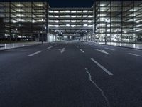 a empty empty city road at night with street lights shining behind it and an illuminated garage on the left side of the road