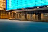 street scene with empty city sidewalk and brightly lit building at night with no cars in front