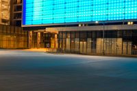 street scene with empty city sidewalk and brightly lit building at night with no cars in front