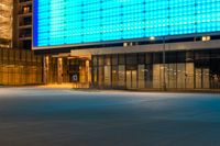 street scene with empty city sidewalk and brightly lit building at night with no cars in front