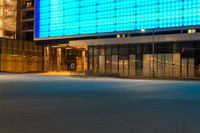 street scene with empty city sidewalk and brightly lit building at night with no cars in front