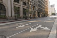 empty city street with large building and arrows painted on the sidewalk area for traffic to enter the intersection