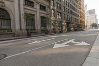 empty city street with large building and arrows painted on the sidewalk area for traffic to enter the intersection