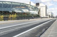 an empty city street near a metal fence with white lines on it, with a green building in the background