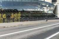 an empty city street near a metal fence with white lines on it, with a green building in the background