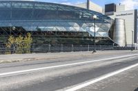 an empty city street near a metal fence with white lines on it, with a green building in the background