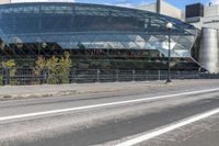 an empty city street near a metal fence with white lines on it, with a green building in the background