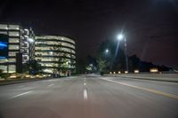 an empty city street lit by the lights of a nearby building at night time with motion blur