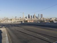an empty city street with the view of a city on one side of it, and traffic lights in the other side