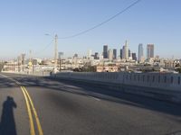 an empty city street with the view of a city on one side of it, and traffic lights in the other side