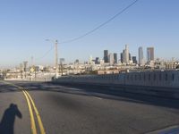 an empty city street with the view of a city on one side of it, and traffic lights in the other side