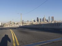 an empty city street with the view of a city on one side of it, and traffic lights in the other side