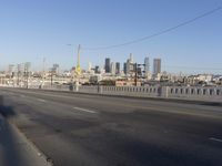 an empty city street with the view of a city on one side of it, and traffic lights in the other side