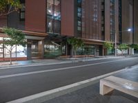 a very empty city street next to a tall building with trees on each side of the road