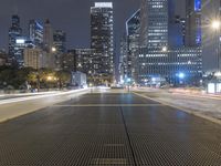 an empty city street with city lights and grates on the ground and buildings in the background