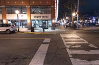 an empty city street at night near a store front with signs reading bright ideas and a van in the street