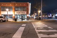 an empty city street at night near a store front with signs reading bright ideas and a van in the street