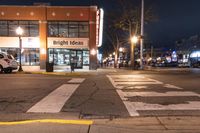 an empty city street at night near a store front with signs reading bright ideas and a van in the street