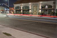 an empty city street at night with a red fire hydrant and a white building