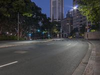 empty road next to trees and buildings at night with green street lights illuminating a building in the distance