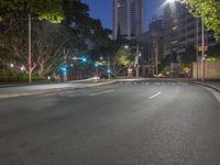 empty road next to trees and buildings at night with green street lights illuminating a building in the distance