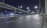 an empty city street at night with lights on the bridges and street lamps above it