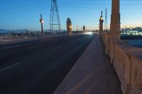 a city street that is empty at night with lights shining on it at sunset near a bridge