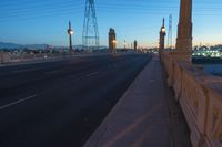 a city street that is empty at night with lights shining on it at sunset near a bridge