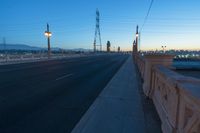 a city street that is empty at night with lights shining on it at sunset near a bridge