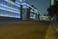 a empty city street at night with tall buildings in the background with lights on in the middle