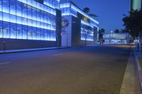 a empty city street at night with tall buildings in the background with lights on in the middle