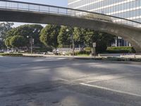 an overpass on an otherwise empty city street, with cars parked and people standing underneath