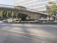 an overpass on an otherwise empty city street, with cars parked and people standing underneath