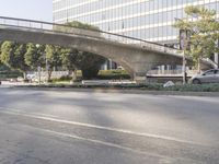 an overpass on an otherwise empty city street, with cars parked and people standing underneath