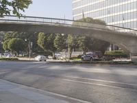 an overpass on an otherwise empty city street, with cars parked and people standing underneath