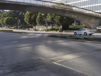 an overpass on an otherwise empty city street, with cars parked and people standing underneath