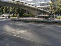 an overpass on an otherwise empty city street, with cars parked and people standing underneath