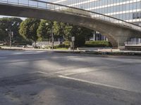 an overpass on an otherwise empty city street, with cars parked and people standing underneath