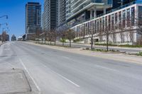 the empty city street has parked cars along side it while traffic moves along the sidewalk