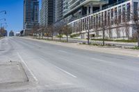 the empty city street has parked cars along side it while traffic moves along the sidewalk