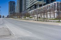 the empty city street has parked cars along side it while traffic moves along the sidewalk