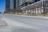 the empty city street has parked cars along side it while traffic moves along the sidewalk