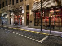 an empty city street at night with red lights and windows and the street lined with street lights