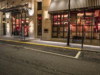 an empty city street at night with red lights and windows and the street lined with street lights