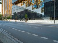 an empty city street next to tall buildings and glassy windows, with some cars parked in the lane and the sidewalk near the curb