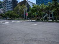 an empty city street has trees and tall buildings in the distance and a red fire hydrant in the middle of the street