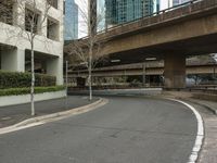 a car on an empty city street under a overpass by a building with tall buildings