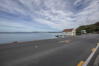 an empty highway with a house by the water near a dock, with two cars parked on it