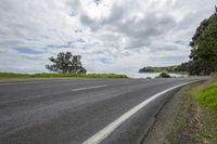 the road by the water looks empty in the daytime sun and cloudy skies above the trees